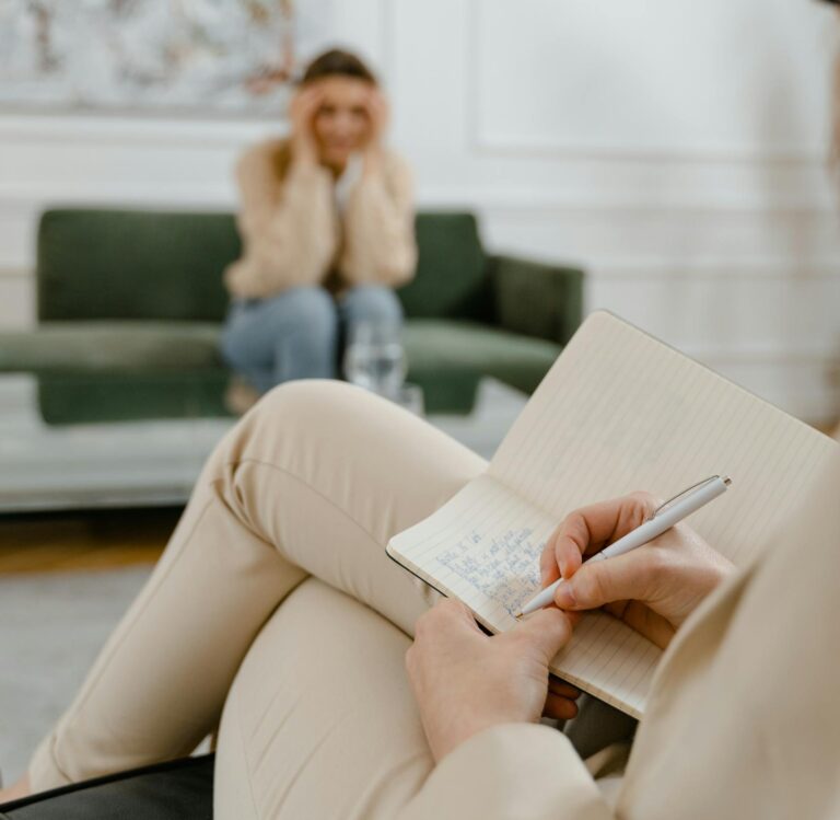 A therapist takes notes in a modern office setting during a therapy session with a patient.
