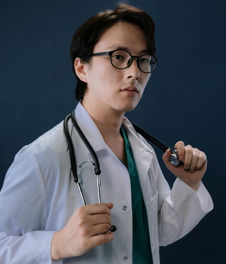 Portrait of a young male doctor in white coat with stethoscope in studio setting.