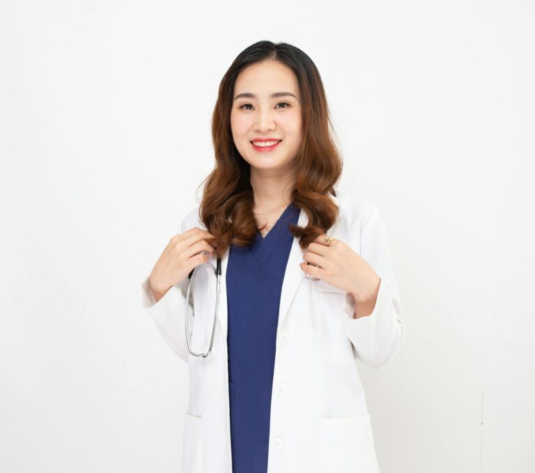 Professional female doctor in scrubs and lab coat smiling confidently on white background.