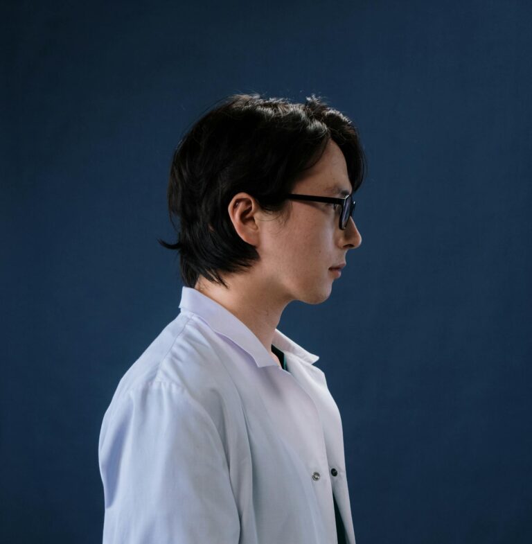 Side profile of an adult male doctor in a white coat against a dark background.