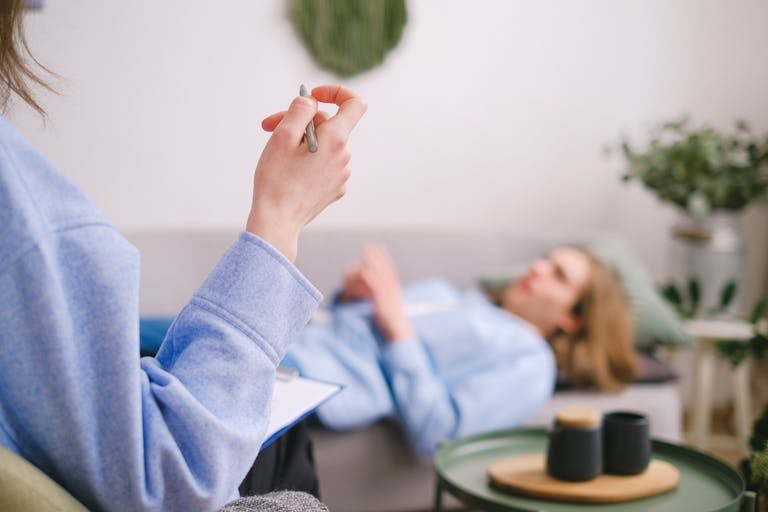 Therapist taking notes during a therapy session with a relaxed client lying on a couch.